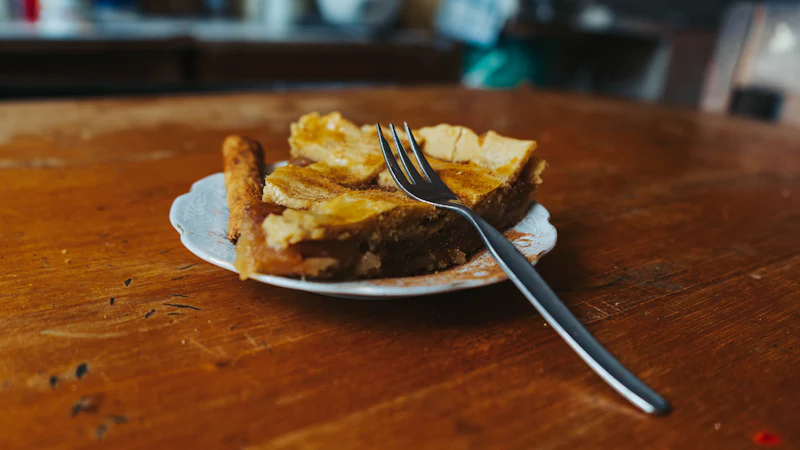 A slice of lattice-top pie on a small plate with a fork, on a wooden table