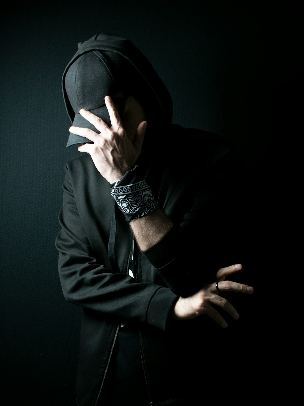 a man in a black hoodie covering his face with his hands