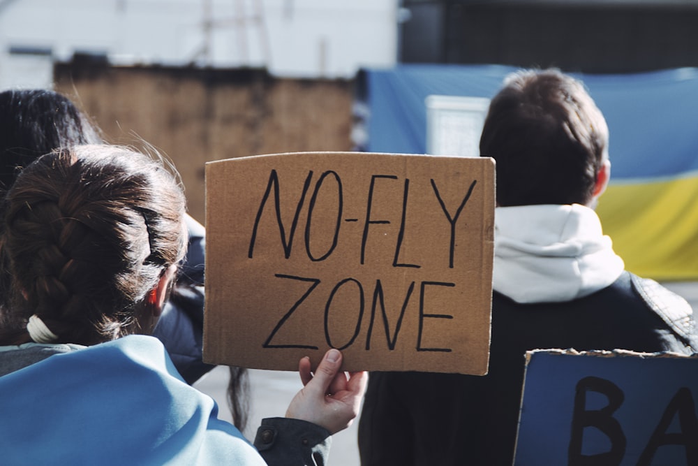 a person holding a sign that says no fly zone