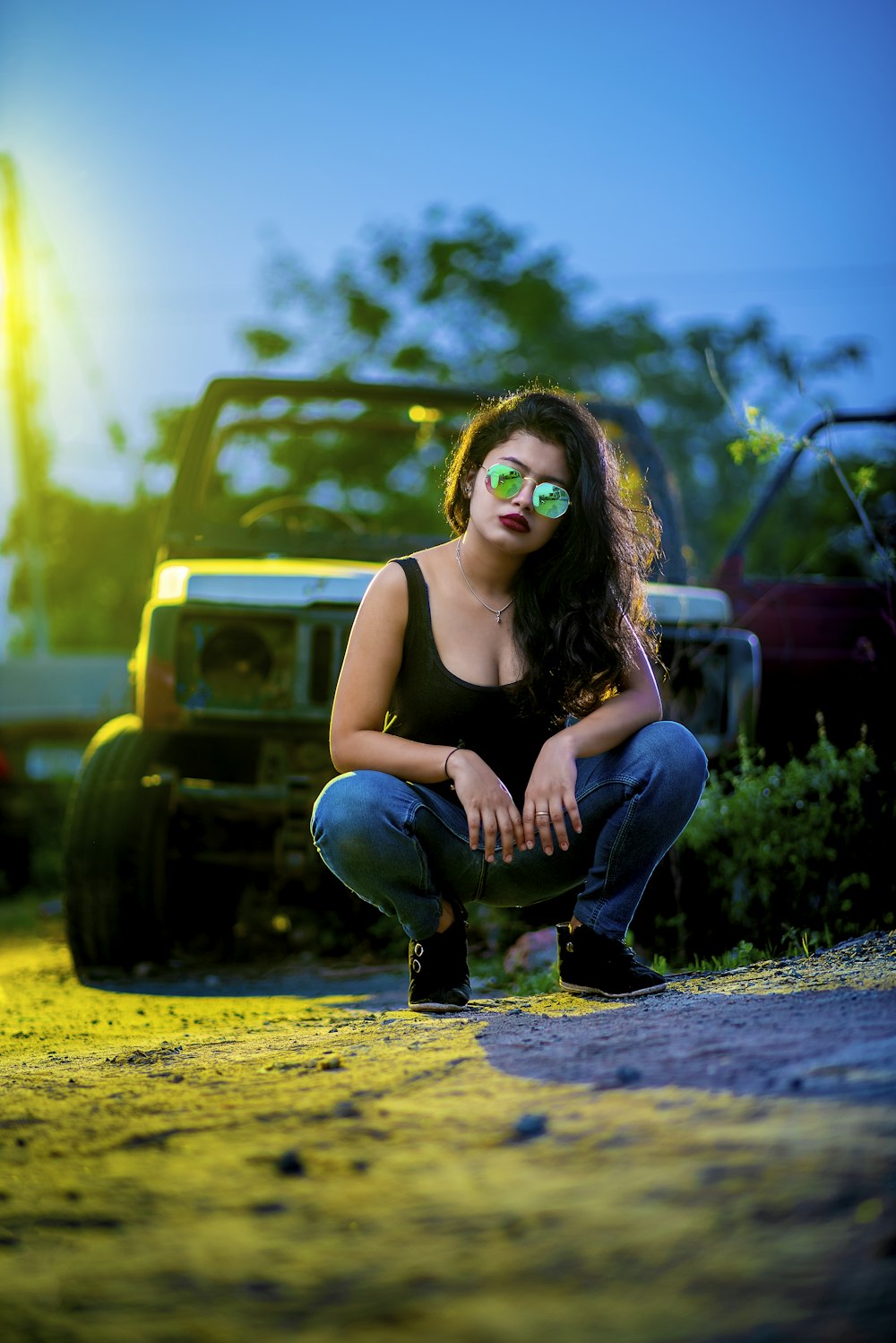 a woman in a black tank top and jeans crouching in front of a truck