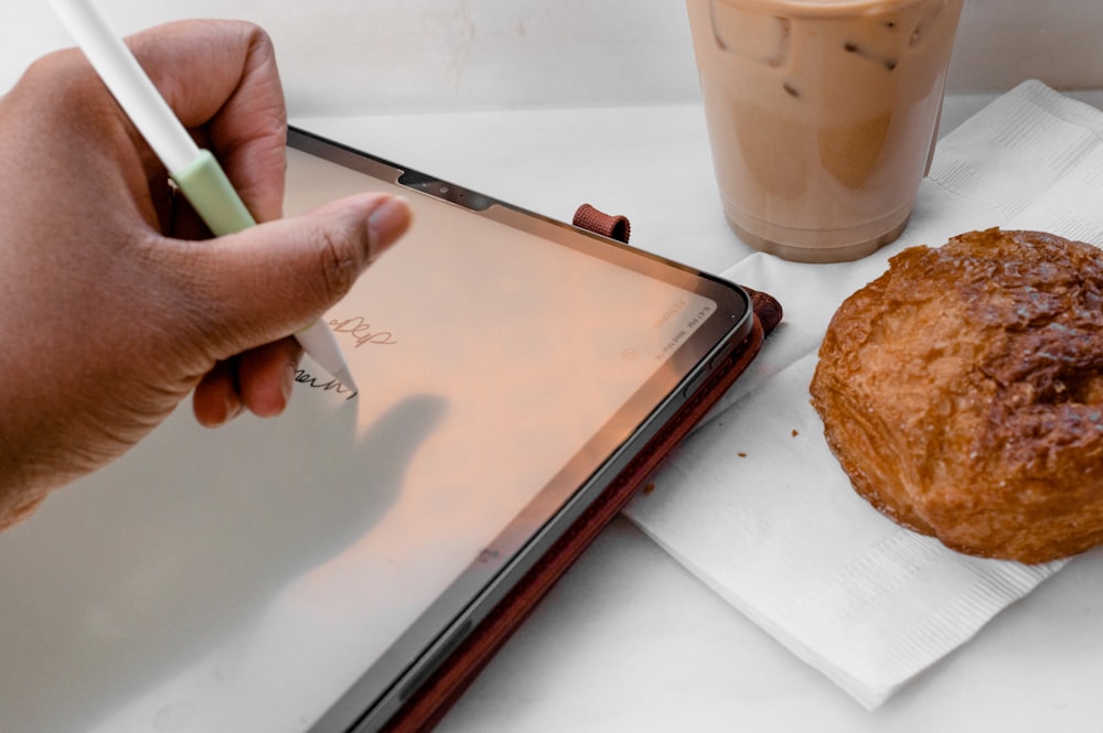 a person writing on a tablet next to a pastry