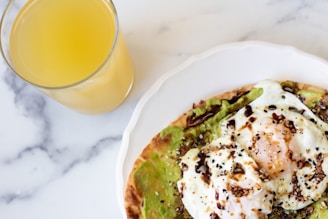 Avocado toast topped with cherry tomatoes and microgreens, served on a white plate with a side of fresh orange juice.