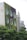 The building facade is covered with lush green vegetation, featuring round windows that resemble portholes. The structure appears modern and eco-friendly, with surrounding trees adding to the verdant atmosphere. Another building in the background complements the urban setting.
