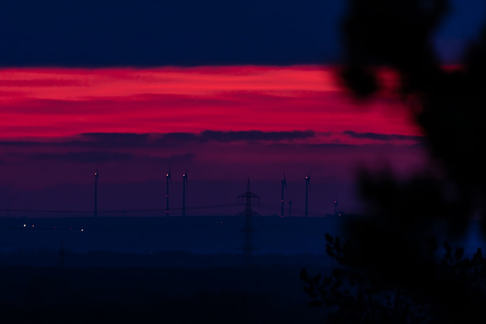 a red and blue sky with a line of wind mills in the distance