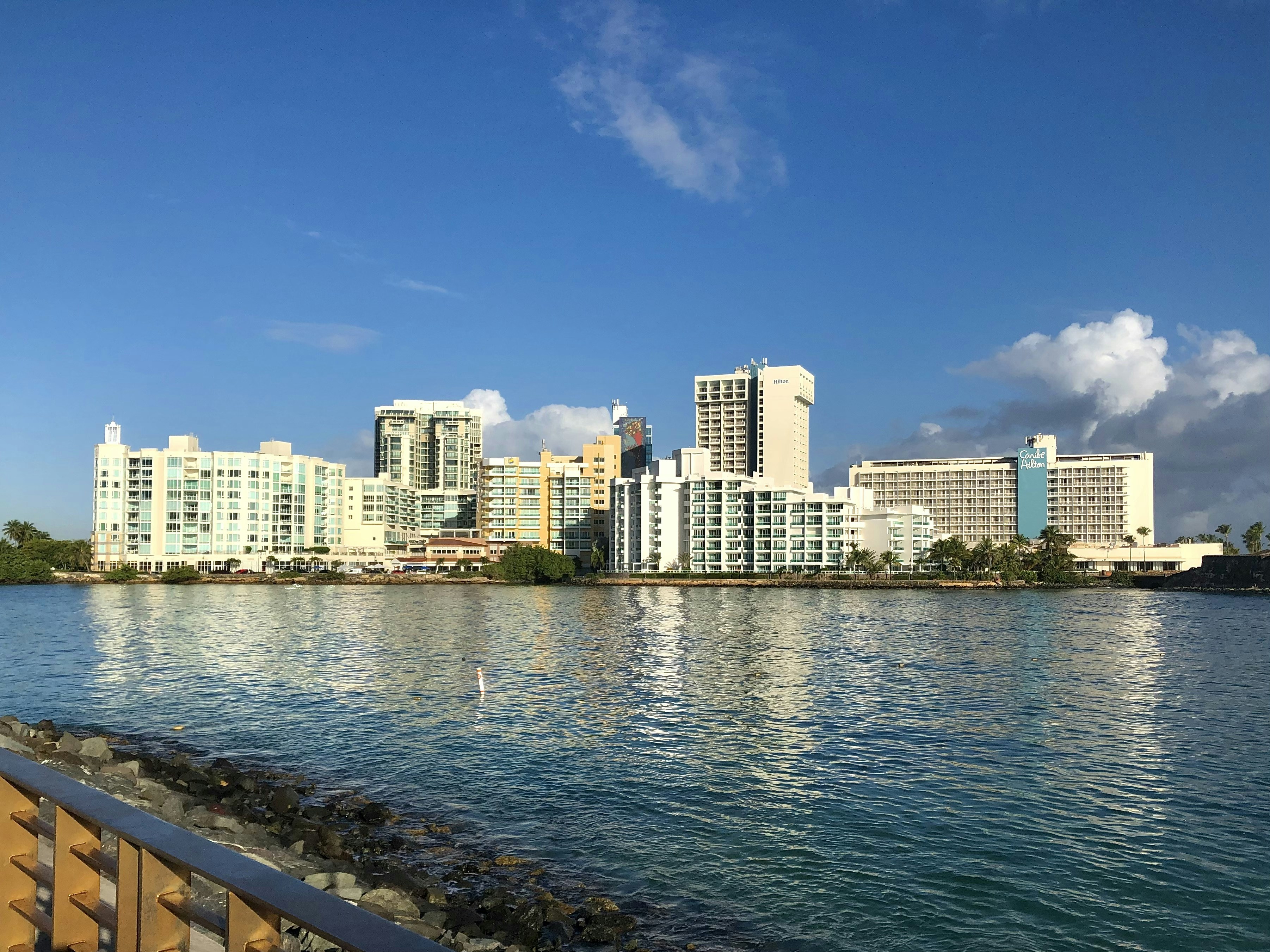 Waterfront view of Condado's modern buildings with reflections on the water, set against a clear blue sky.