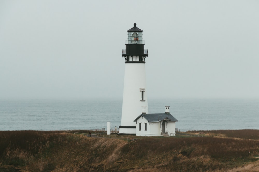 a white and black light house on a grassy hill