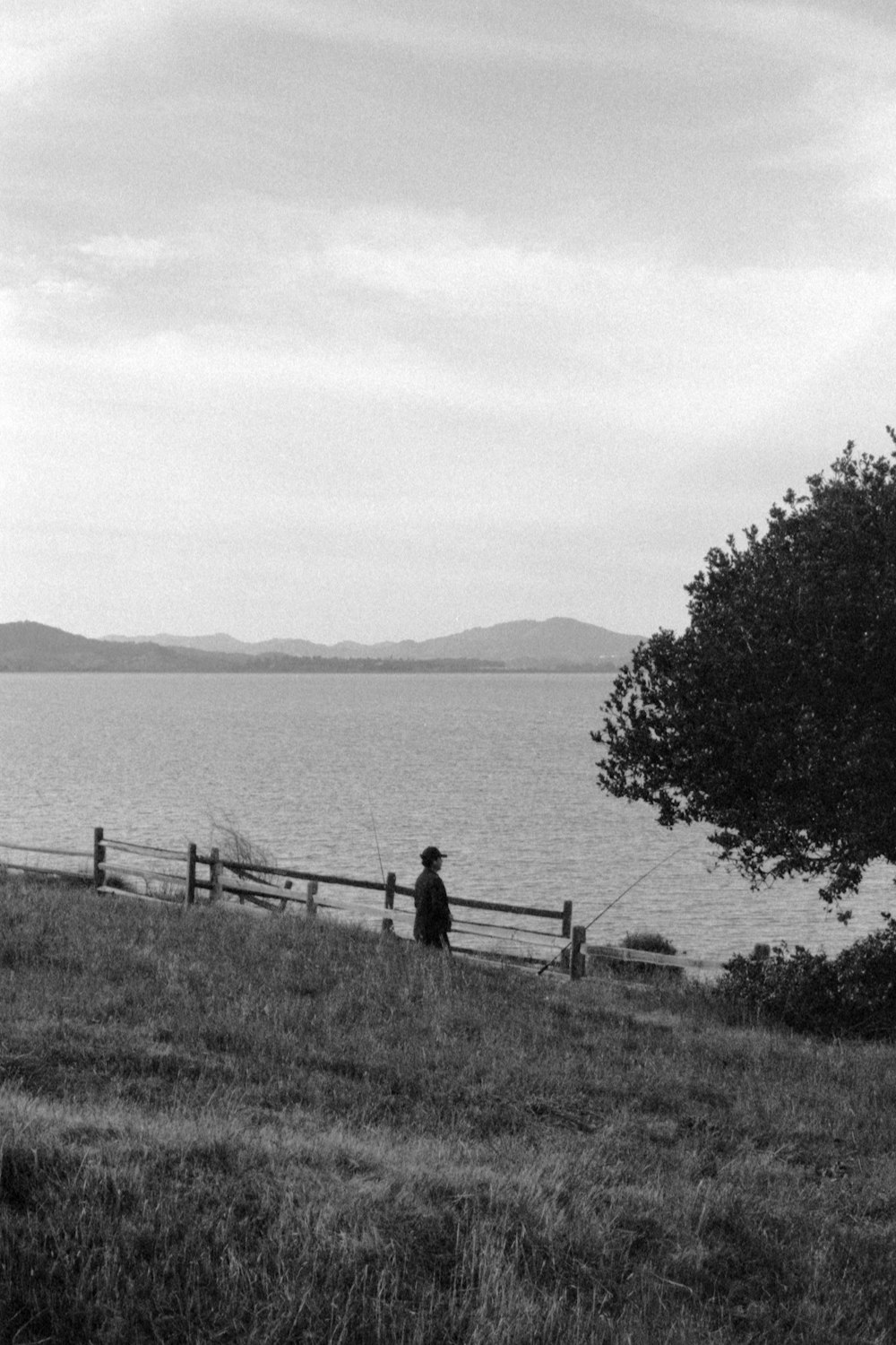 a black and white photo of a person sitting on a bench by the water
