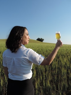 a woman standing in a field holding a glass of beer