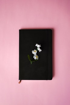 a black notebook with white flowers on a pink background