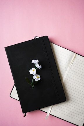 A close-up of a blush pink journal open on a cream white table, surrounded by honey yellow wildflowers.