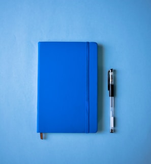 a blue notebook and a pen on a blue surface