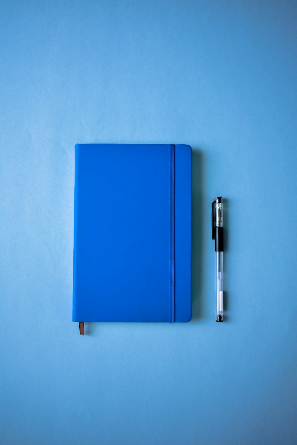 a blue notebook and a pen on a blue surface