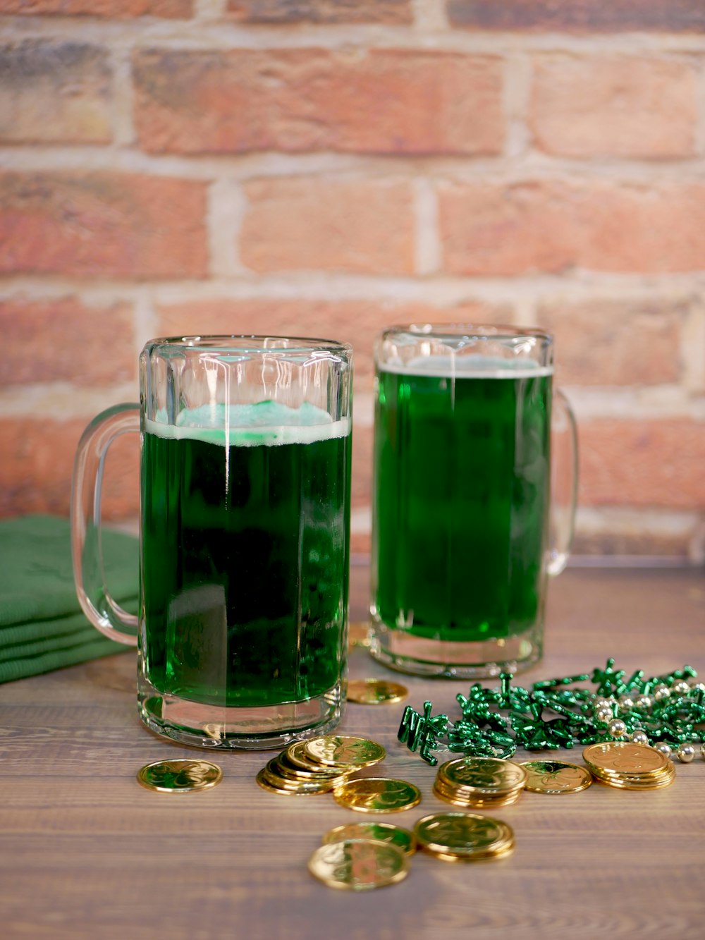 two mugs filled with green liquid next to gold coins