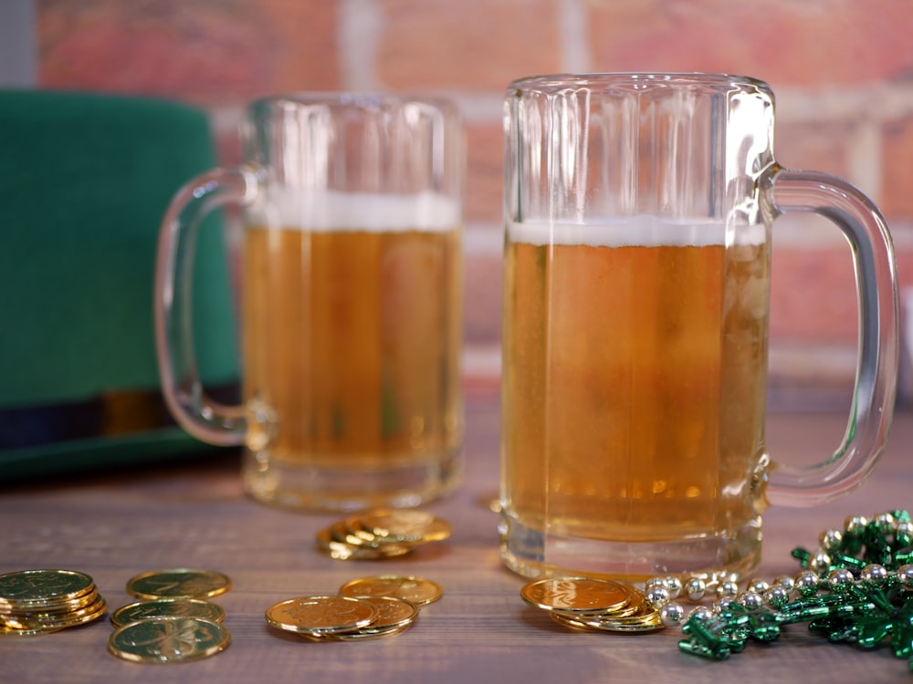 two mugs filled with beer next to gold coins