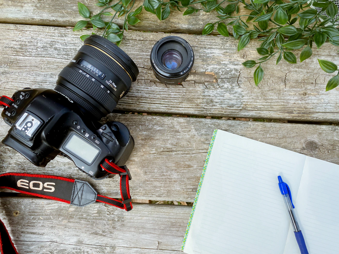 Camera, spare lens, open notebook and pen on a wooden table
