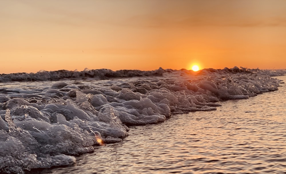 the sun is setting over the ocean with foamy waves