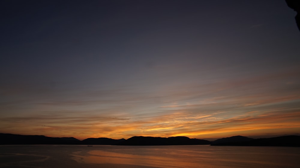 Ein Sonnenuntergang über einem Gewässer mit Bergen im Hintergrund