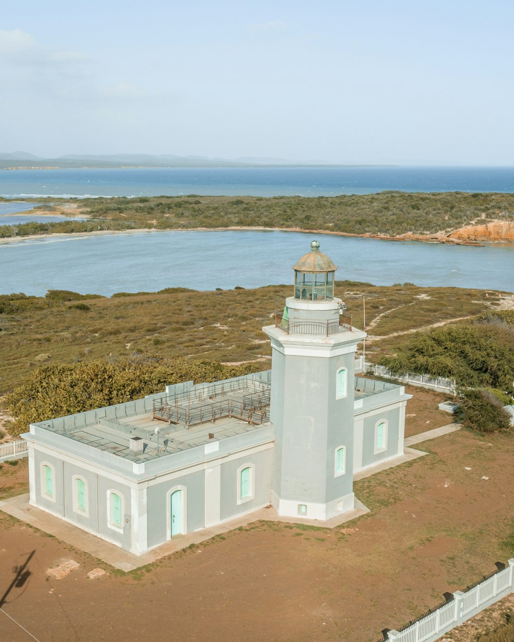 an aerial view of a white lighthouse with a body of water in the background