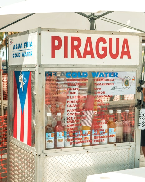 picture of piragua cart displaying flavor options, colored glass bottles, and a puerto rican flag decal on the side window