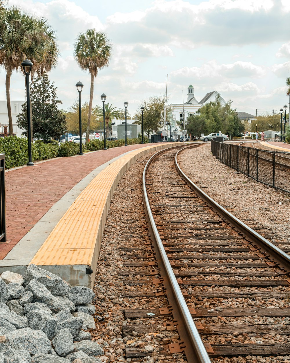a train track with a light pole and palm trees in the background