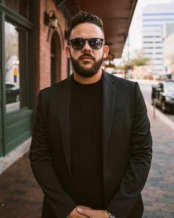 a man in a suit and sunglasses standing on a sidewalk