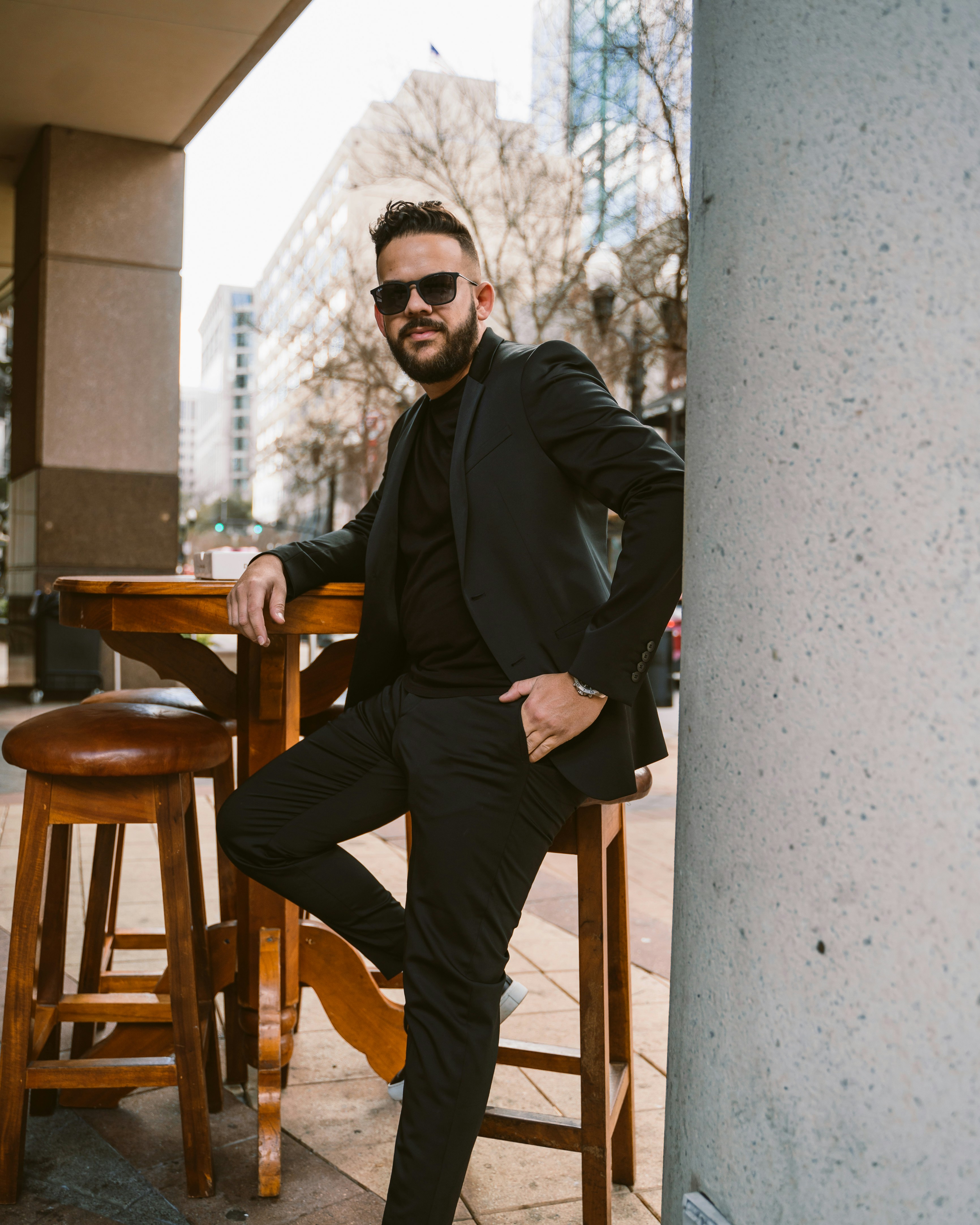 a man in a suit and sunglasses sitting on a stool
