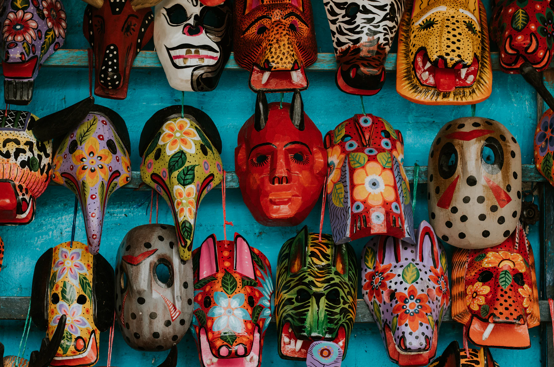 Rows of painted wooden jaguar, devil and animal masks hung on a turquoise wall