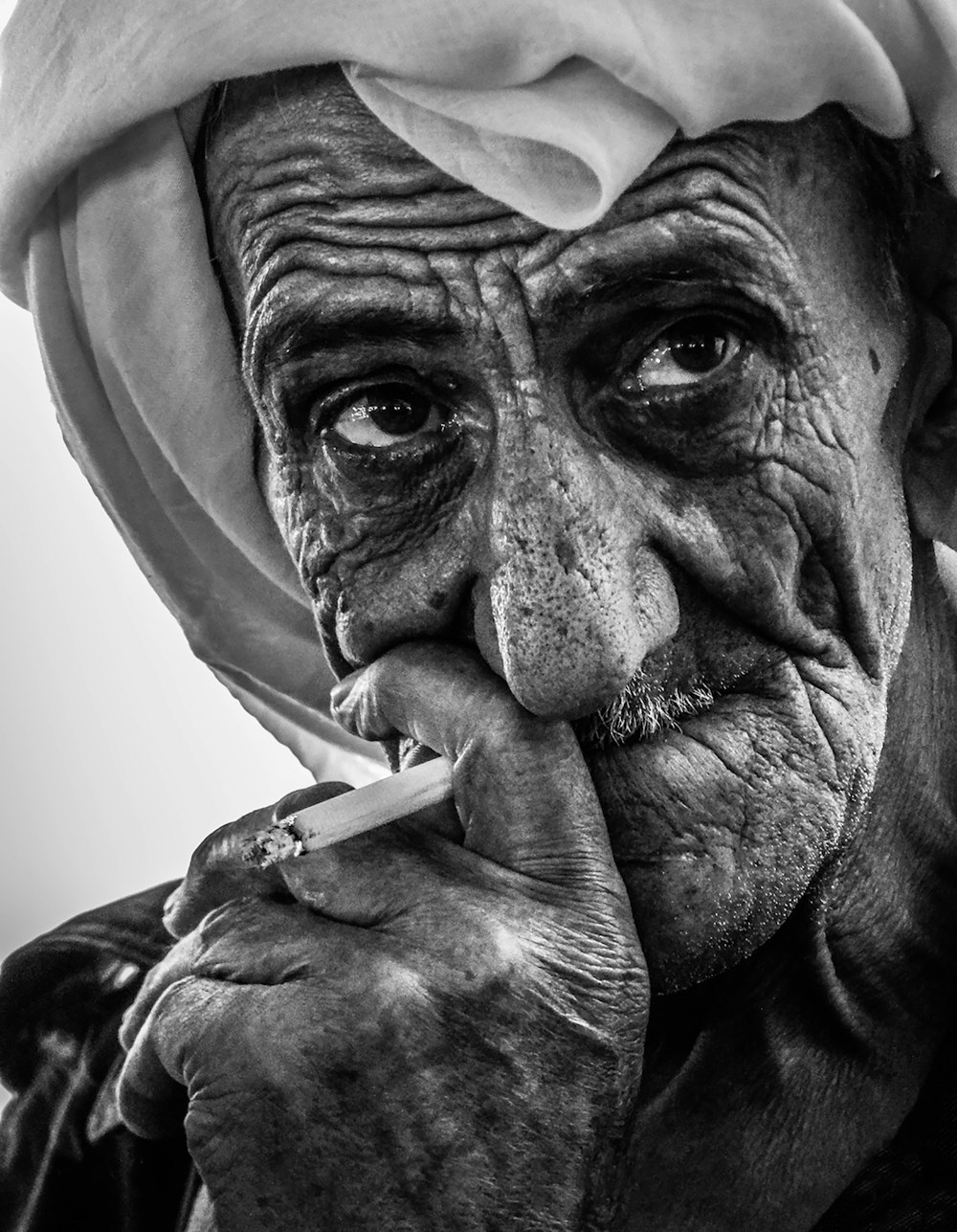 a black and white photo of an old man smoking a cigarette