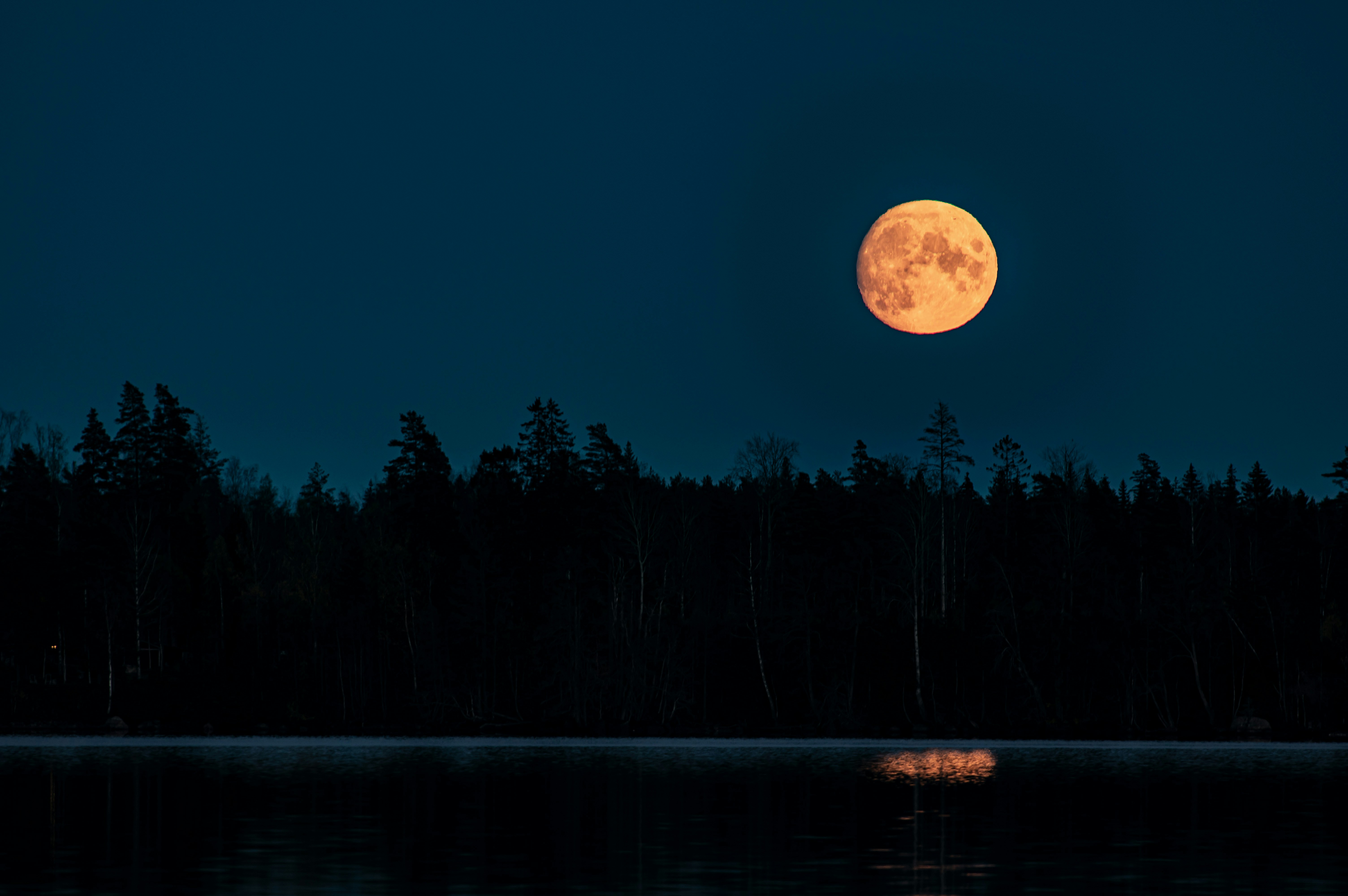 a full moon is seen over a lake