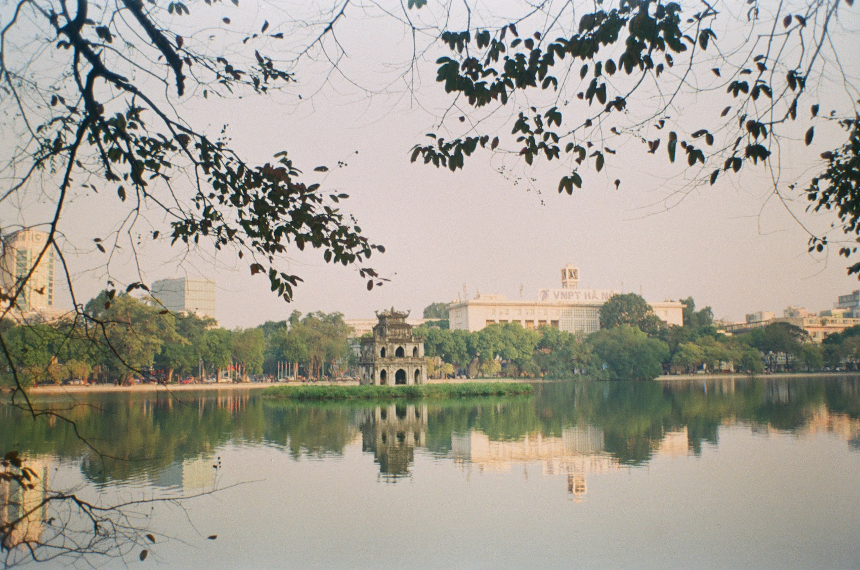 A calm Hanoi lake framed by branches in hazy seasonal light