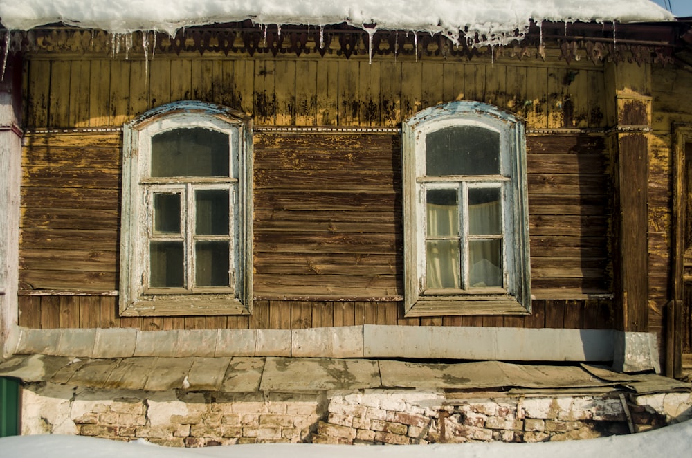 an old wooden house with three windows and snow on the roof