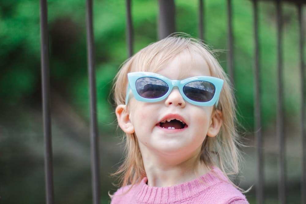 Una niña con gafas de sol azules y un suéter rosa