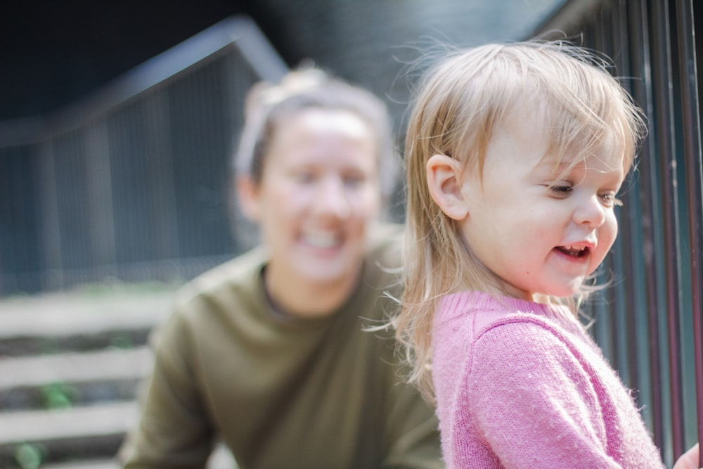 a woman and a little girl playing with a fence