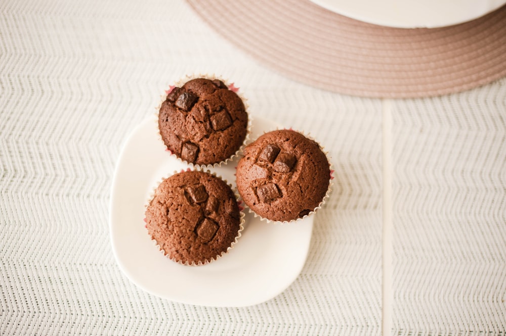three chocolate muffins sitting on a white plate