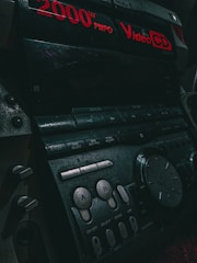 Close-up of a vintage audio system with red digital text displaying '2000W PMPO' and 'Video CD'. Various buttons and dials are visible, including controls labeled 'A' and 'B'. The lighting is dim, accentuating the retro aesthetics of the device.