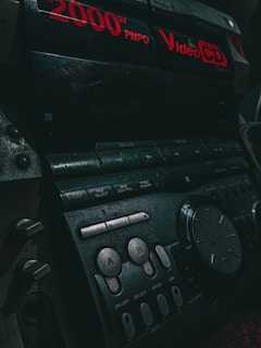 Close-up of a vintage audio system with red digital text displaying '2000W PMPO' and 'Video CD'. Various buttons and dials are visible, including controls labeled 'A' and 'B'. The lighting is dim, accentuating the retro aesthetics of the device.