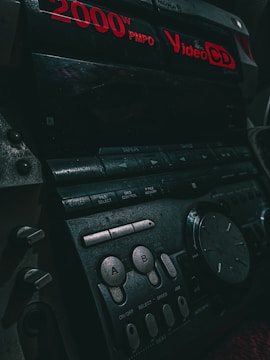 Close-up of a vintage audio system with red digital text displaying '2000W PMPO' and 'Video CD'. Various buttons and dials are visible, including controls labeled 'A' and 'B'. The lighting is dim, accentuating the retro aesthetics of the device.