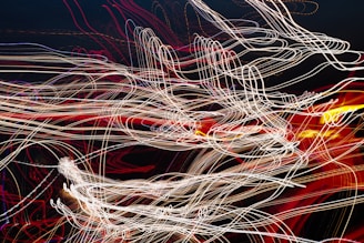A complex network of swirling, intertwined light trails in various colors against a dark background, creating an abstract and dynamic visual effect.