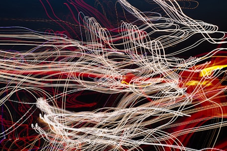 A complex network of swirling, intertwined light trails in various colors against a dark background, creating an abstract and dynamic visual effect.