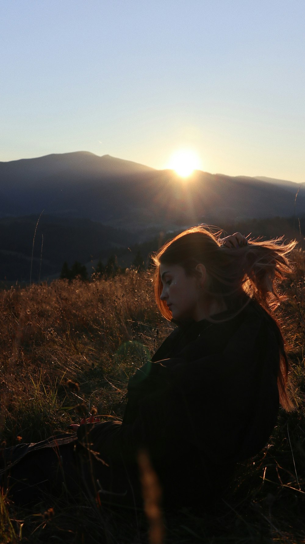 a woman sitting on top of a grass covered hillside