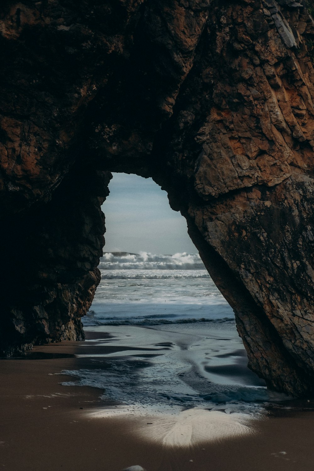 a large rock sticking out of the ocean next to a beach