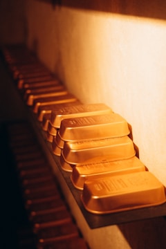 A row of neatly arranged gold bars on a shelf, illuminated by warm lighting, creating a luxurious and rich ambiance.