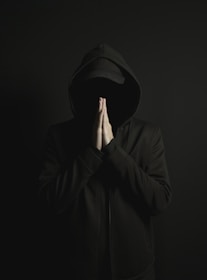 a man in a black hoodie is covering his face with his hands