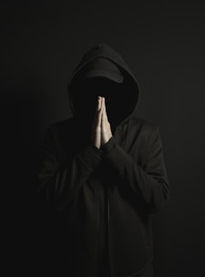 a man in a black hoodie is covering his face with his hands