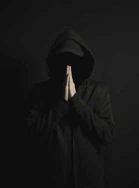 a man in a black hoodie is covering his face with his hands