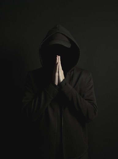 a man in a black hoodie is covering his face with his hands