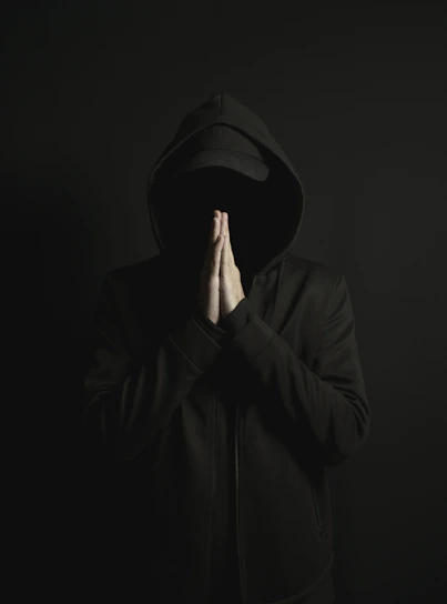 a man in a black hoodie is covering his face with his hands
