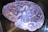 A translucent, sculpted model of a human brain, showing intricate grooves and folds. The surface has a glossy sheen, reflecting light in various shades of purple and blue, giving it a surreal, almost ethereal appearance.