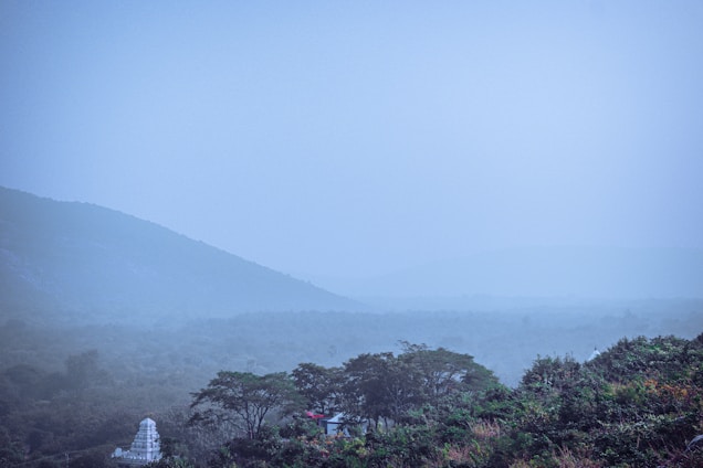 A tranquil early morning view of misty mountain peaks surrounding a cozy Navira Hills lodge.