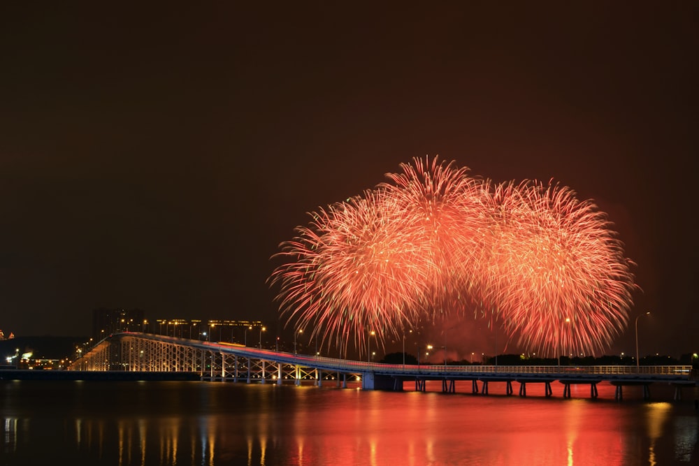 a firework display over a body of water with a bridge in the background